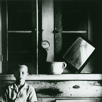 Black and white photo of a boy, clock and mirror in an old house.